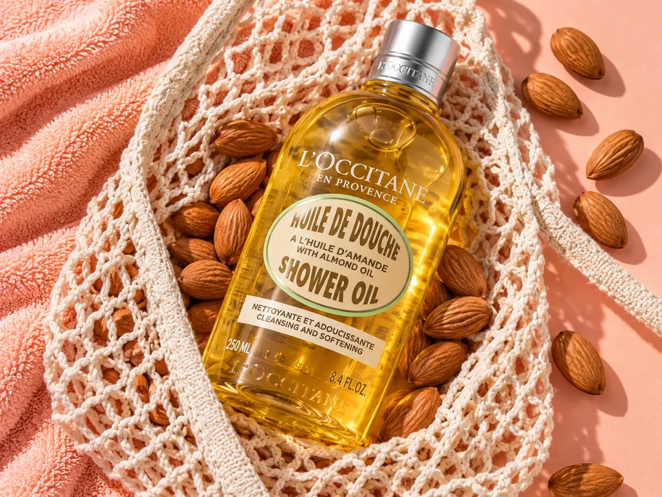 Bottle of L’Occitane shower oil in a cotton net bag among almonds on a pink towel